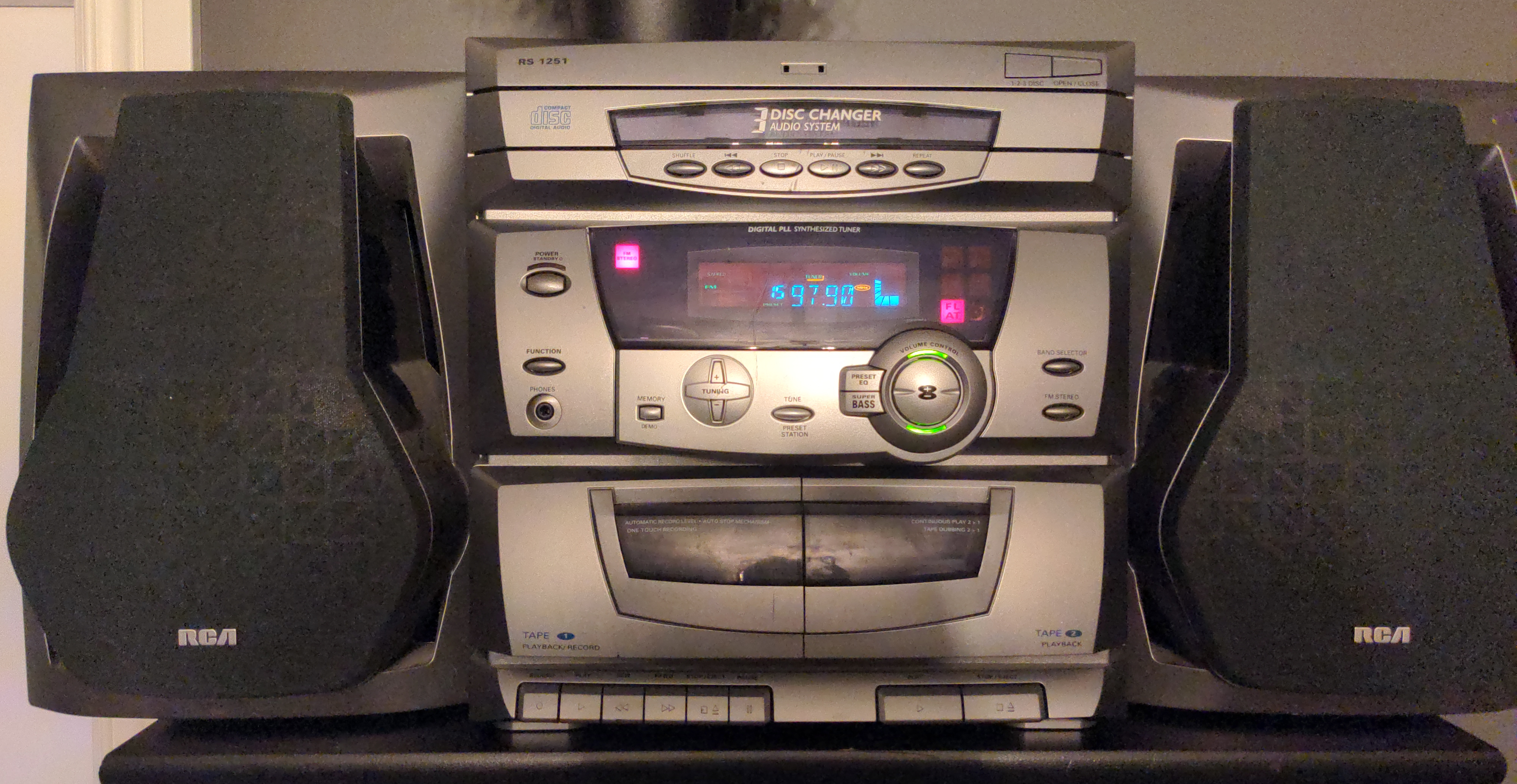 A turn-of-the-century RCA home stereo system consisting of two bookshelf speakers and a central unit featuring a 3-disc CD changer, an AM/FM radio, and dual tape decks for dubbing, as well as five EQ presets and a "Super Bass" button.
