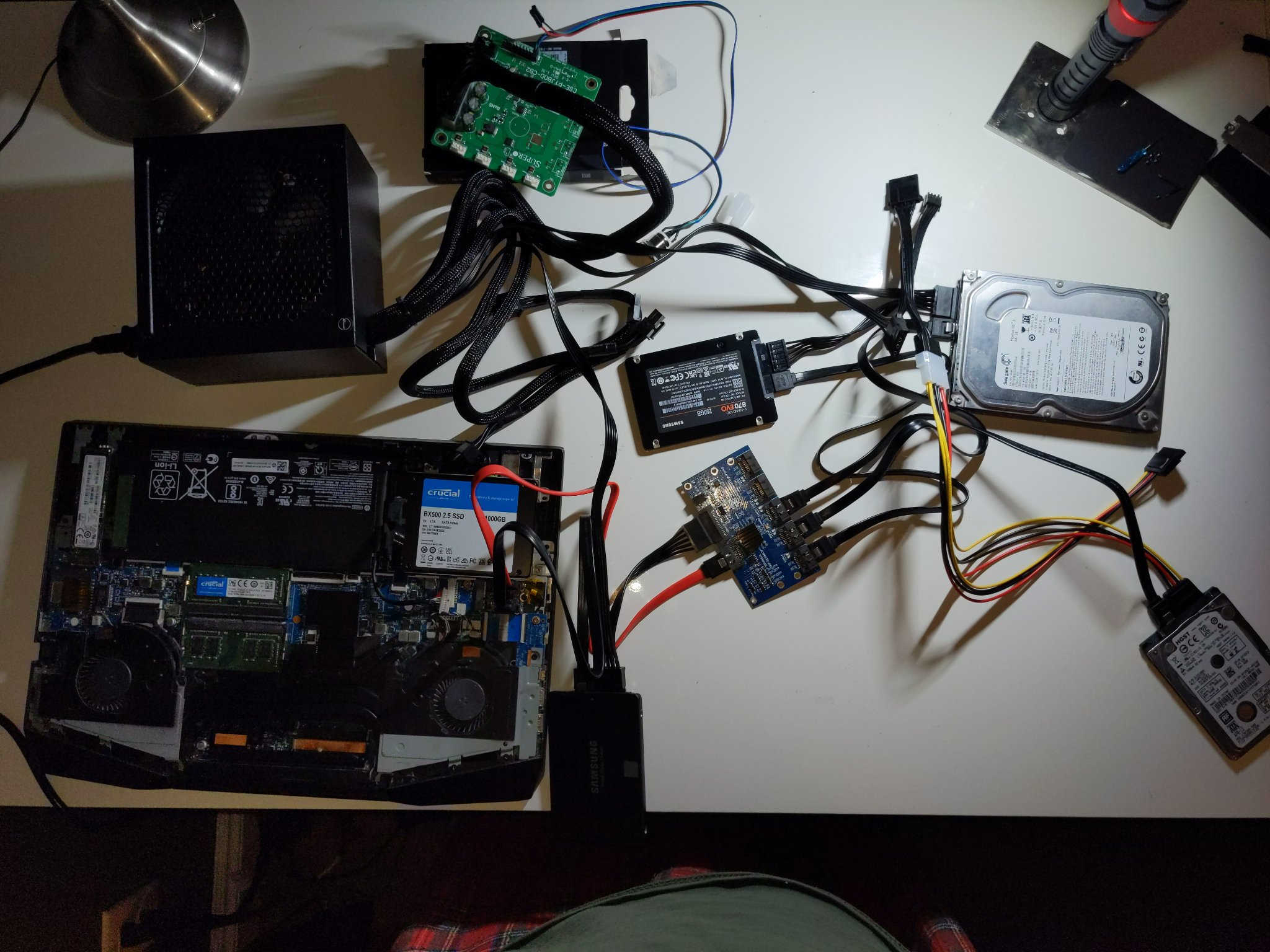 Five SATA drives plugged into a laptop, one via an internal SATA bay, and the other four via an M.2 SATA controller in place of the WiFi card and a SATA splitter board. The latter four hard drives are powered off of an ATX PC PSU controlled by a Supermicro JBOD controller board.