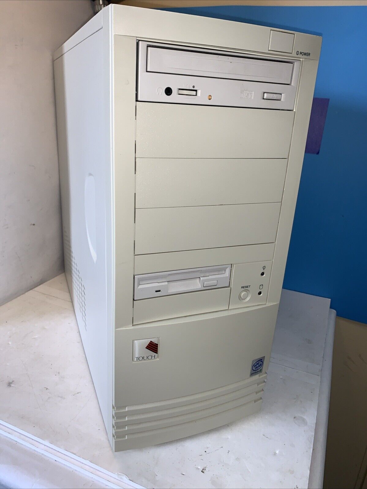 A beige PC tower with four 5.25" bays and two external 3.5" bays, populated with an optical drive and a floppy drive respectively. The only visible branding is a Pentium III sticker and a badge that reads "TOUCH".