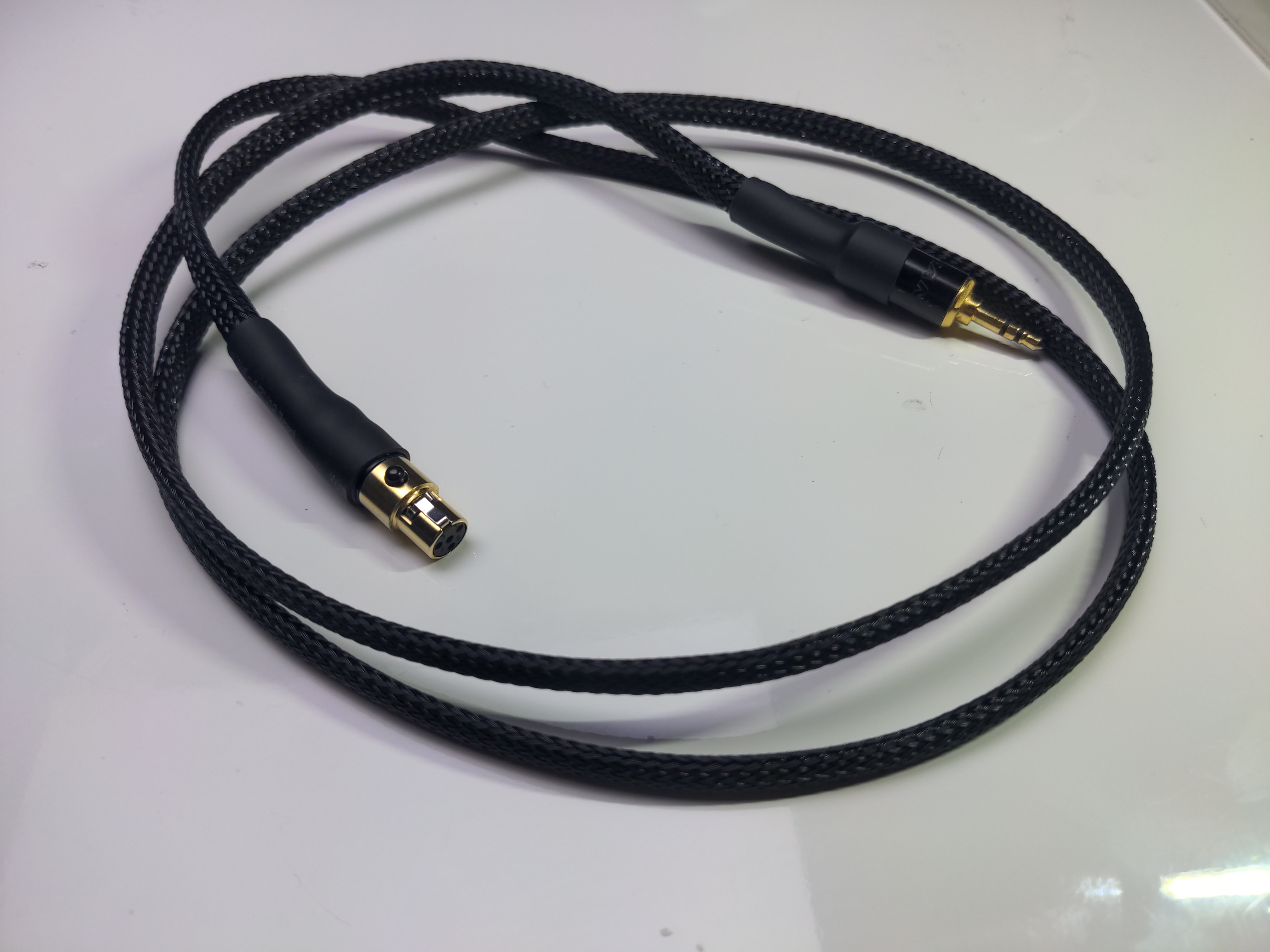 A 3.5mm jack to 4-pin mini XLR adapter cable with a shiny black braided exterior